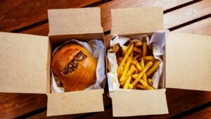 Overhead view of a burger and fries in eco-friendly paper boxes on a wooden table.